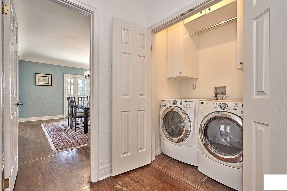 Inspiration for a mid-sized traditional single-wall dedicated laundry room in Los Angeles with a single-bowl sink, raised-panel cabinets, white cabinets, laminate benchtops, white walls, medium hardwood floors, a concealed washer and dryer, brown floor and white benchtop.