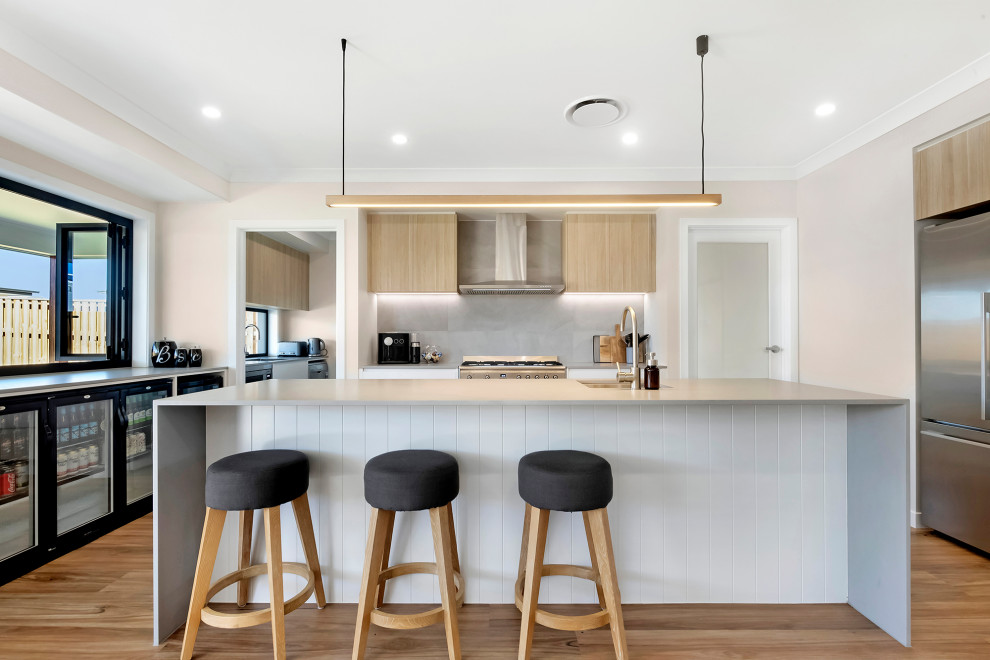 Inspiration for a contemporary u-shaped kitchen in Gold Coast - Tweed with an undermount sink, flat-panel cabinets, light wood cabinets, grey splashback, stainless steel appliances, medium hardwood floors, with island, brown floor and white benchtop.