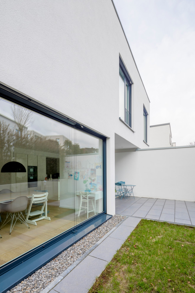 Idée de décoration pour une façade de maison blanche design en stuc de taille moyenne et à un étage avec un toit plat.