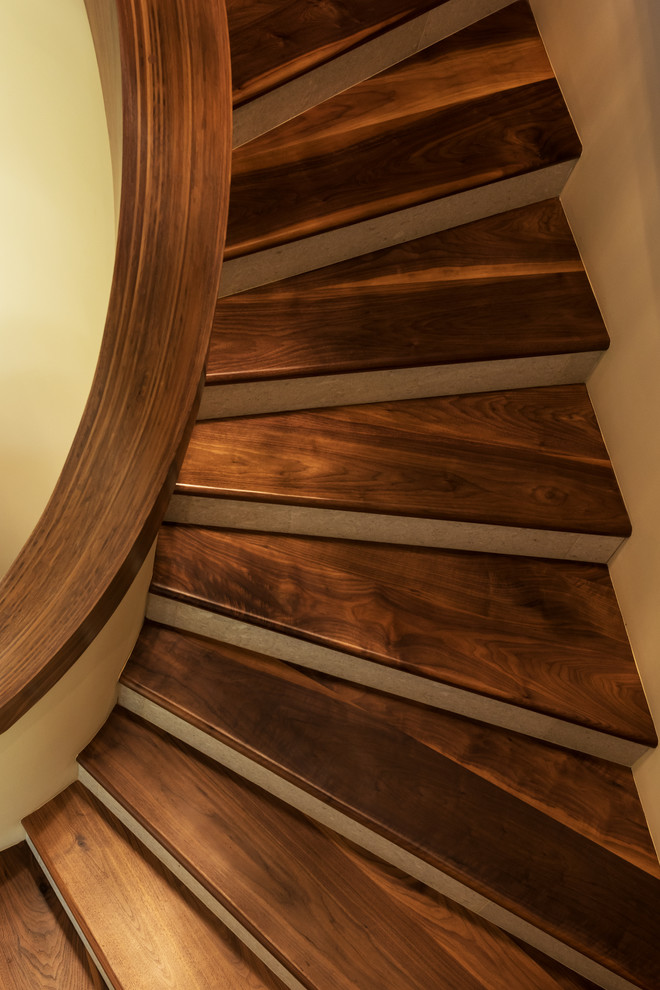 Стильный дизайн: изогнутая лестница в современном стиле с деревянными ступенями, подступенками из известняка и деревянными перилами - последний тренд