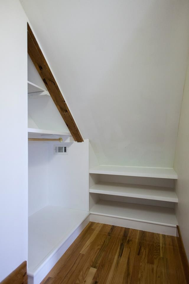 This is an example of a small country gender-neutral walk-in wardrobe in Portland Maine with light hardwood floors, open cabinets and white cabinets.