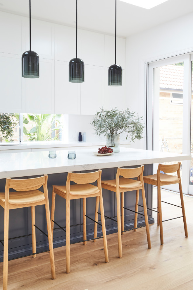 Design ideas for a traditional l-shaped kitchen in Sydney with shaker cabinets, blue cabinets, quartz benchtops, white splashback, engineered quartz splashback, light hardwood floors and with island.
