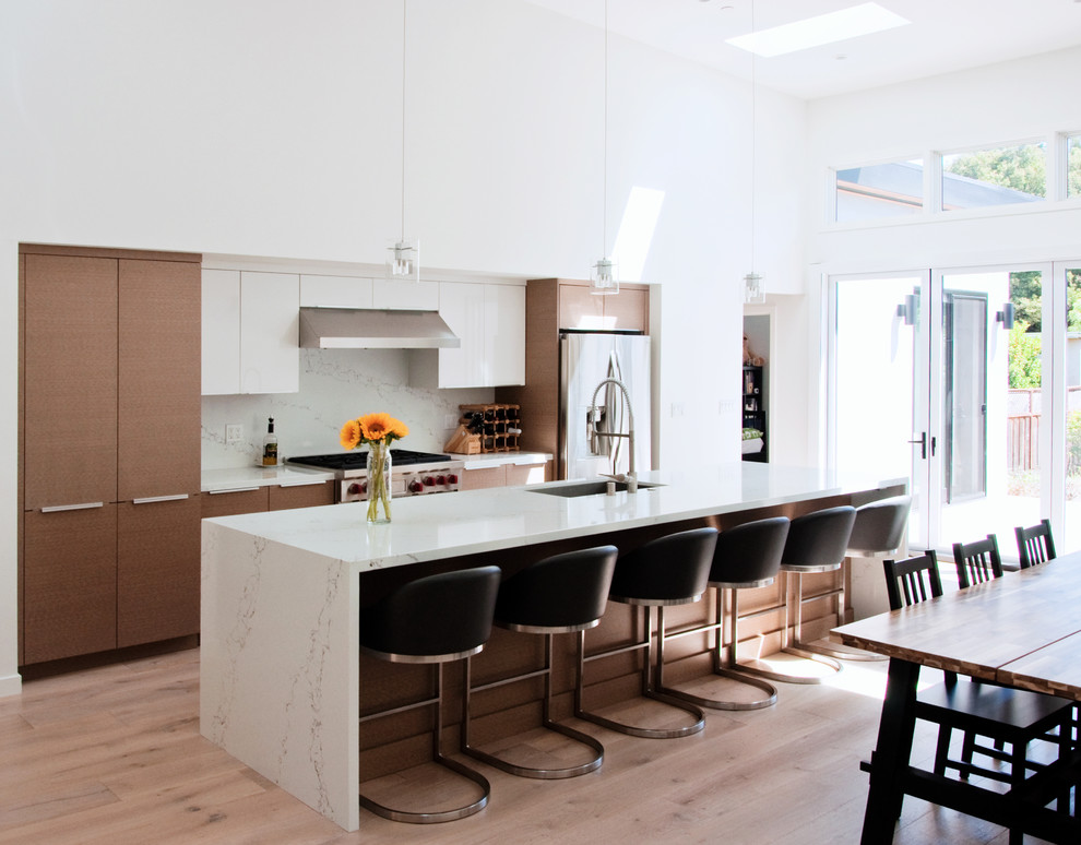 Photo of a mid-sized modern single-wall open plan kitchen in San Francisco with an undermount sink, flat-panel cabinets, medium wood cabinets, quartz benchtops, white splashback, stone slab splashback, stainless steel appliances, light hardwood floors, with island, brown floor and white benchtop.