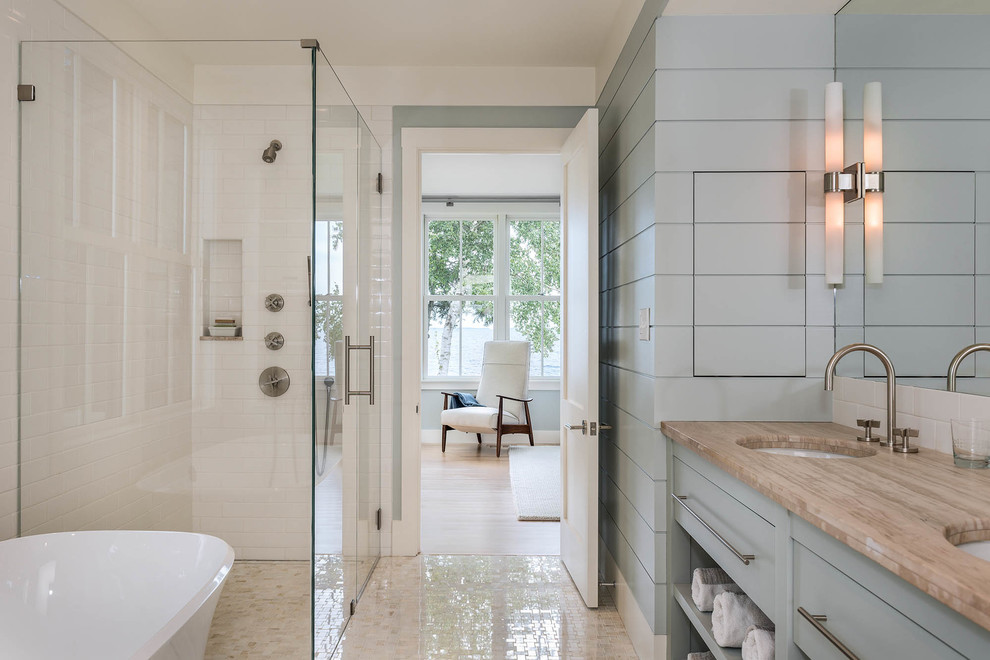 Design ideas for a large beach style master bathroom in Portland Maine with flat-panel cabinets, blue cabinets, a curbless shower, white tile, subway tile, blue walls, an undermount sink, a freestanding tub, marble floors, granite benchtops and a hinged shower door.