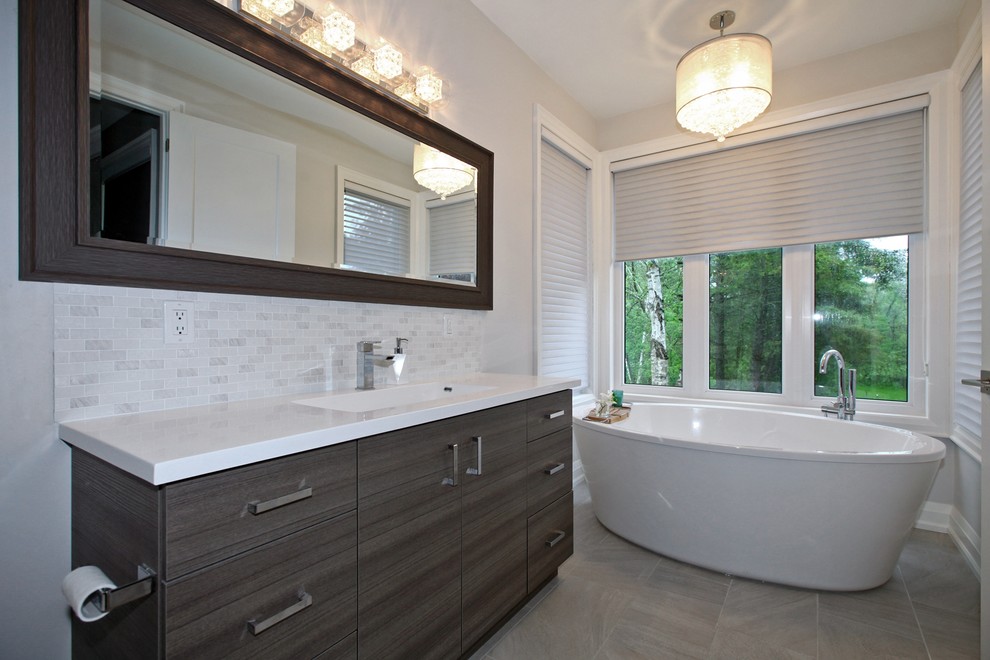 Inspiration for a mid-sized transitional master bathroom in Toronto with flat-panel cabinets, dark wood cabinets, a freestanding tub, a one-piece toilet, gray tile, white tile, matchstick tile, grey walls, porcelain floors, an undermount sink, solid surface benchtops and grey floor.