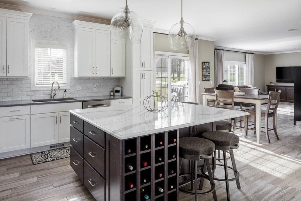 Example of a mid-sized transitional l-shaped ceramic tile and gray floor eat-in kitchen design with an undermount sink, shaker cabinets, white cabinets, quartz countertops, white backsplash, marble backsplash, stainless steel appliances, an island and gray countertops