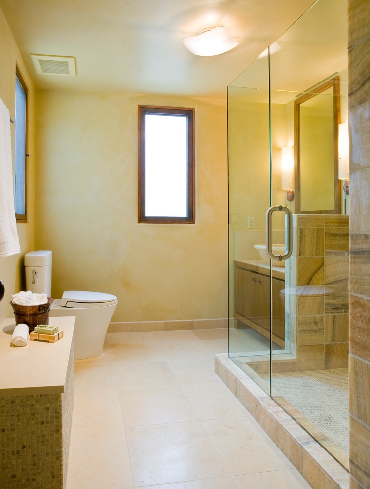Photo of a large tropical 3/4 bathroom in Santa Barbara with flat-panel cabinets, medium wood cabinets, a corner shower, a two-piece toilet, brown tile, ceramic tile, beige walls, ceramic floors, a vessel sink, engineered quartz benchtops, beige floor, a hinged shower door and beige benchtops.
