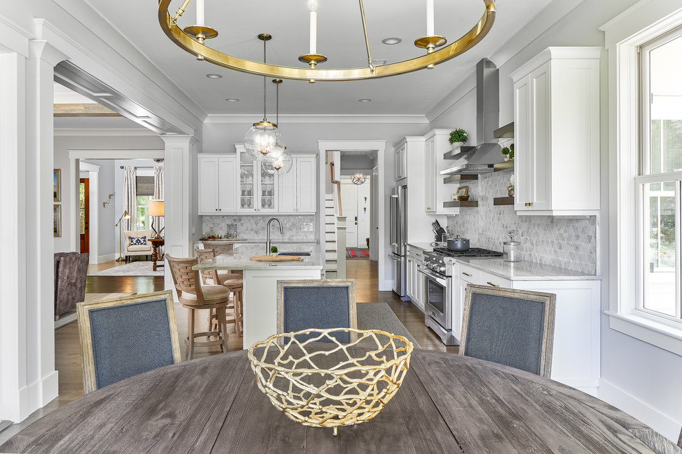 Large beach style u-shaped eat-in kitchen in Charleston with grey splashback, stainless steel appliances, with island, a drop-in sink, white cabinets, quartzite benchtops, mosaic tile splashback, dark hardwood floors, brown floor and white benchtop.