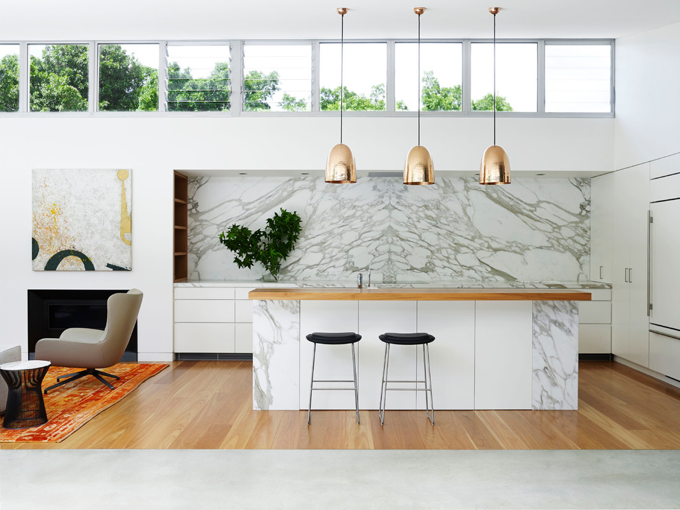 Expansive contemporary open plan kitchen in Sydney with flat-panel cabinets, white cabinets, marble benchtops, with island, white splashback and panelled appliances.