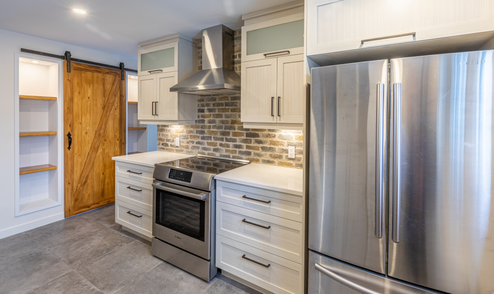 This is an example of a large contemporary galley open plan kitchen in Montreal with a single-bowl sink, shaker cabinets, beige cabinets, quartzite benchtops, grey splashback, brick splashback, ceramic floors, with island, grey floor and white benchtop.