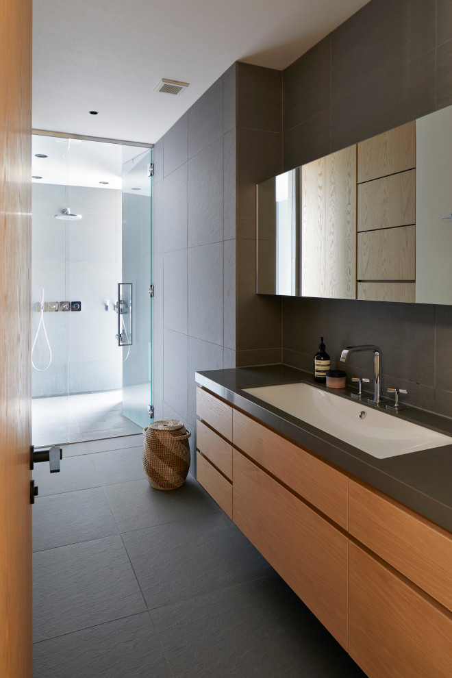 This is an example of a contemporary bathroom in Other with flat-panel cabinets, medium wood cabinets, a curbless shower, gray tile, an undermount sink, grey floor, a hinged shower door, grey benchtops, a single vanity and a floating vanity.