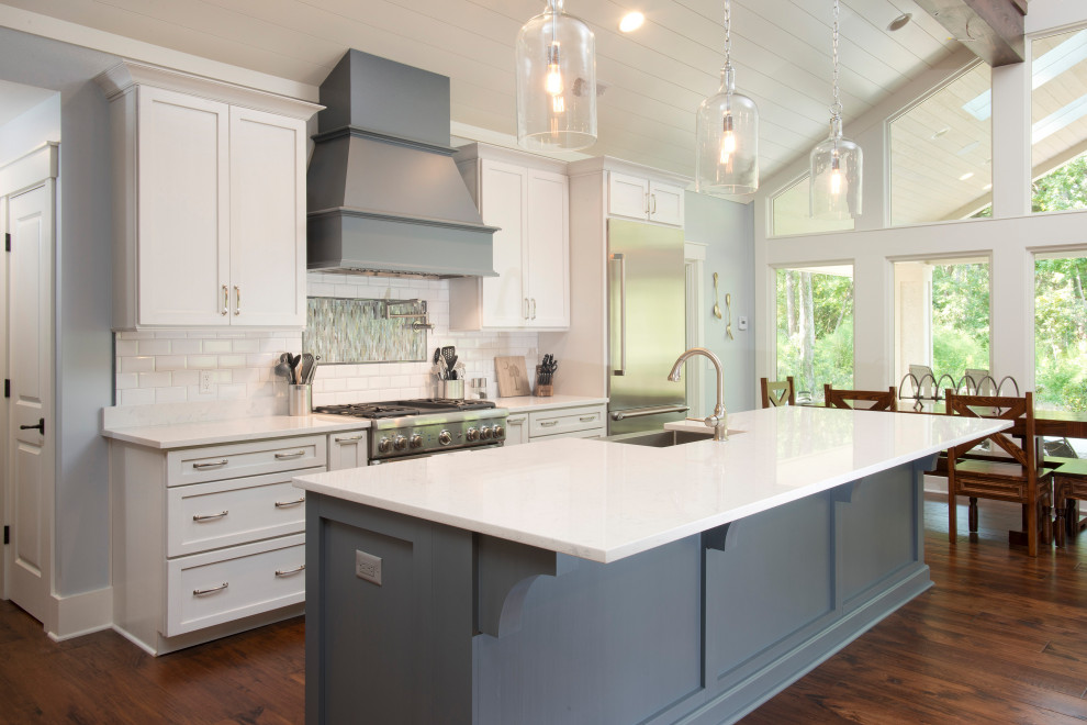Example of a large transitional galley medium tone wood floor and brown floor open concept kitchen design with a farmhouse sink, shaker cabinets, blue cabinets, quartz countertops, white backsplash, ceramic backsplash, stainless steel appliances, an island and white countertops