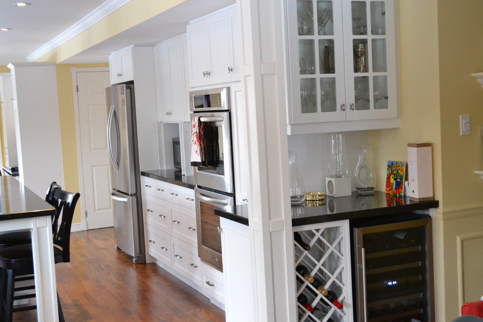 Eat-in kitchen - large transitional galley medium tone wood floor eat-in kitchen idea in Toronto with a double-bowl sink, shaker cabinets, white cabinets, granite countertops, white backsplash, subway tile backsplash, stainless steel appliances and an island