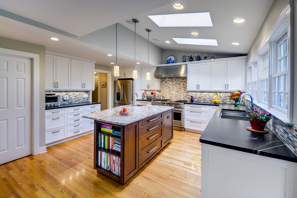 This is an example of a mid-sized traditional l-shaped open plan kitchen in Detroit with an undermount sink, recessed-panel cabinets, white cabinets, soapstone benchtops, grey splashback, ceramic splashback, stainless steel appliances, medium hardwood floors and with island.