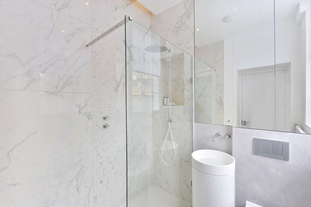 Small contemporary 3/4 bathroom in London with glass-front cabinets, an open shower, a one-piece toilet, gray tile, stone tile, white walls, a pedestal sink and marble benchtops.