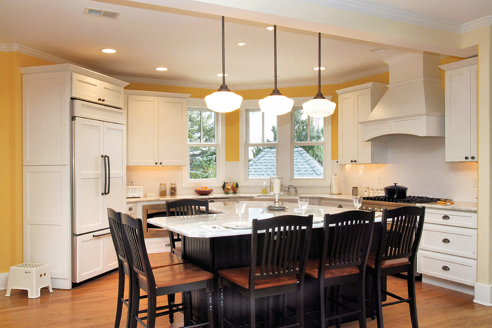 This is an example of a traditional l-shaped eat-in kitchen in New York with shaker cabinets, white cabinets, with island and white benchtop.