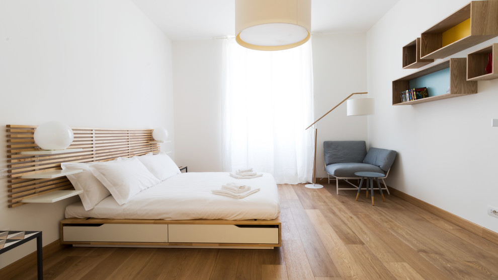 Photo of a contemporary bedroom in Milan with white walls, medium hardwood floors and brown floor.