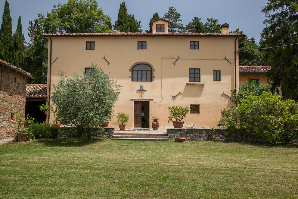 Mediterranean yellow house exterior in Other with a gable roof and a tile roof.