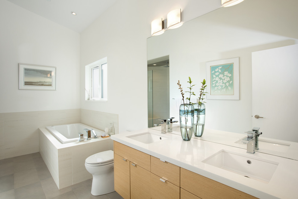 This is an example of a mid-sized modern bathroom in Vancouver with flat-panel cabinets, light wood cabinets, an alcove shower, a one-piece toilet, white tile, ceramic tile, white walls, ceramic floors, an undermount sink and a drop-in tub.