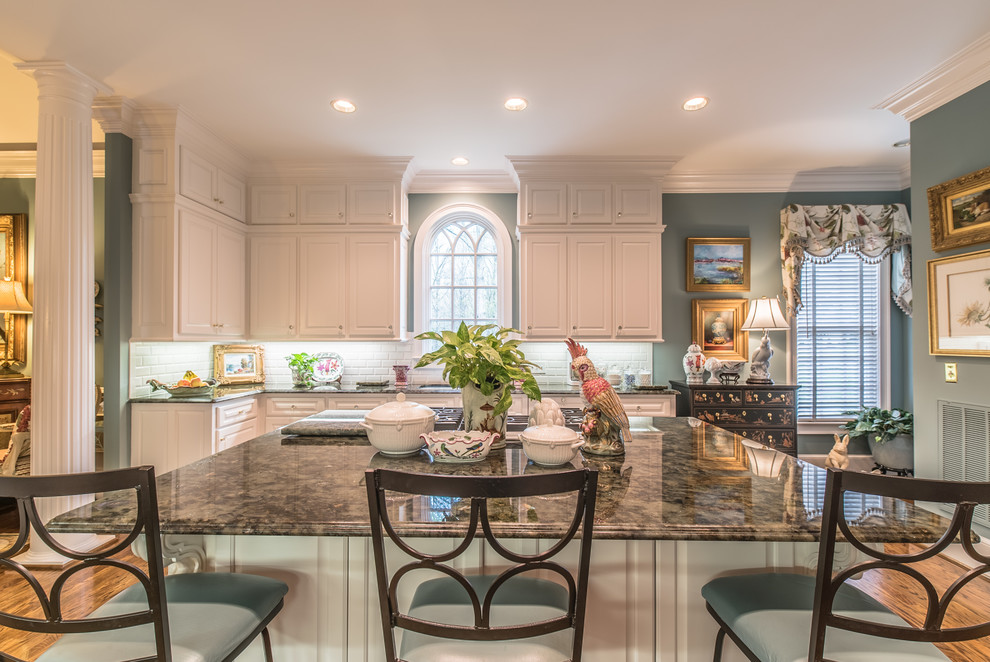 This is an example of an expansive traditional galley open plan kitchen in Charleston with a double-bowl sink, raised-panel cabinets, white cabinets, quartzite benchtops, white splashback, subway tile splashback, white appliances, light hardwood floors and with island.