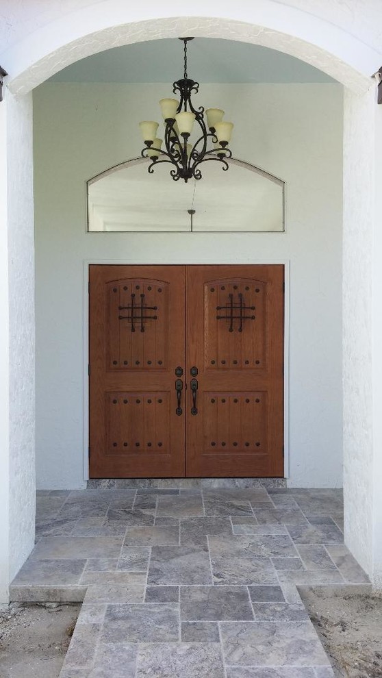 This is an example of a mid-sized mediterranean front door in Miami with white walls, travertine floors, a double front door, a medium wood front door and grey floor.