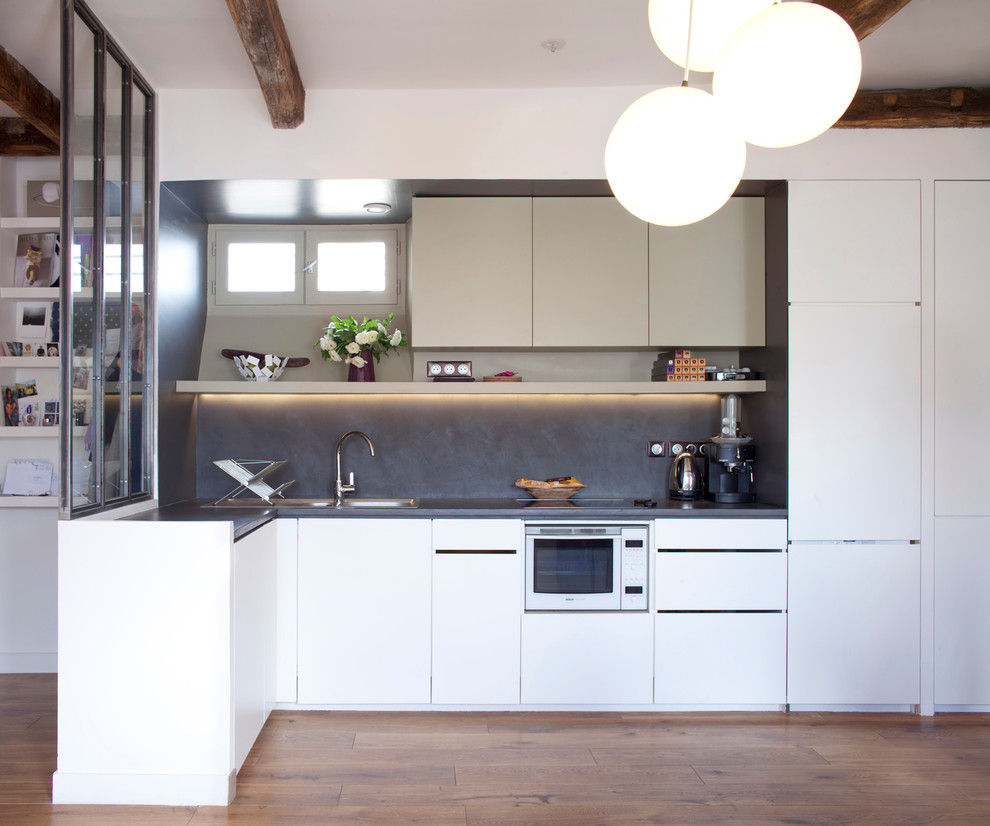 Mid-sized contemporary l-shaped open plan kitchen in Other with a double-bowl sink, flat-panel cabinets, white cabinets, grey splashback, white appliances, medium hardwood floors and a peninsula.