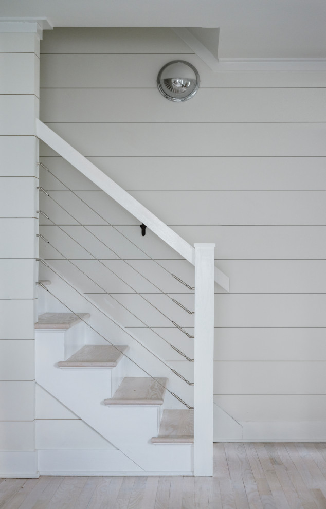 Mid-sized beach style wood straight staircase in Other with painted wood risers, cable railing and planked wall panelling.
