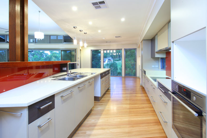 Cette photo montre une grande cuisine ouverte parallèle moderne avec un évier 2 bacs, un placard à porte shaker, des portes de placard blanches, un plan de travail en granite, une crédence rouge, une crédence en carreau de verre, un électroménager en acier inoxydable, parquet clair et îlot.