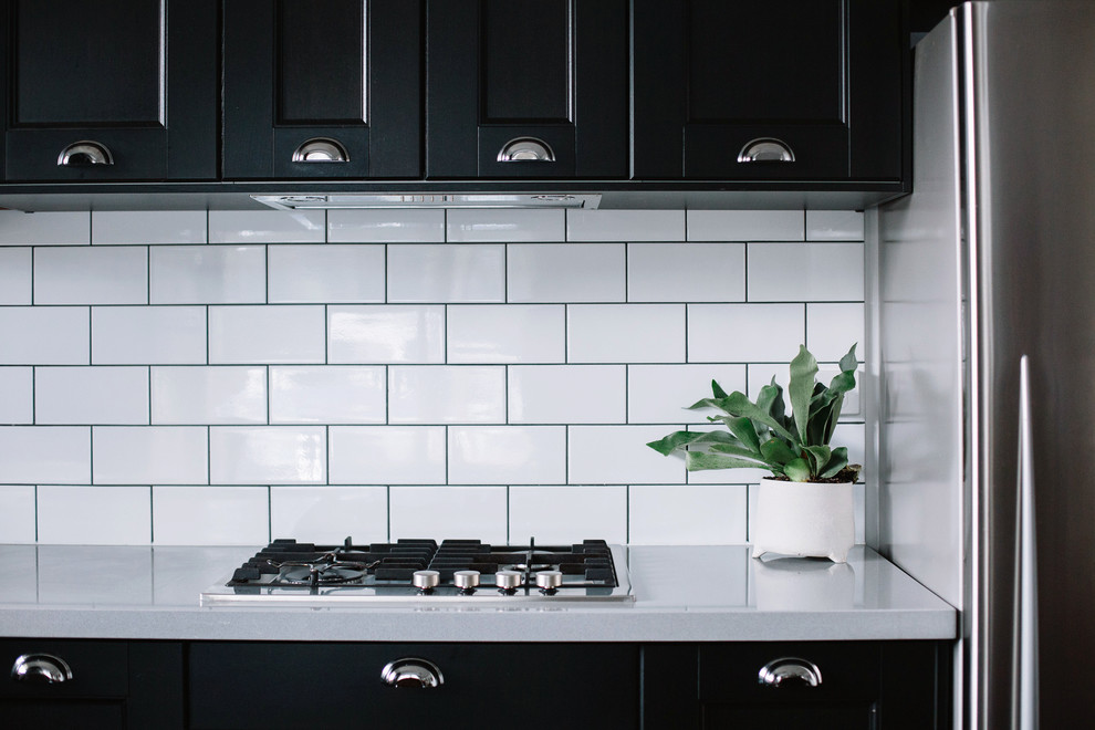 Inspiration for a small transitional l-shaped eat-in kitchen in Perth with a farmhouse sink, recessed-panel cabinets, black cabinets, solid surface benchtops, white splashback, subway tile splashback, stainless steel appliances, dark hardwood floors and no island.