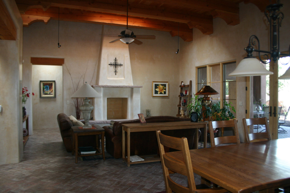 This is an example of a large open plan living room in Albuquerque with beige walls, brick flooring, a standard fireplace, a plastered fireplace surround, no tv, red floors, exposed beams, a vaulted ceiling and a wood ceiling.