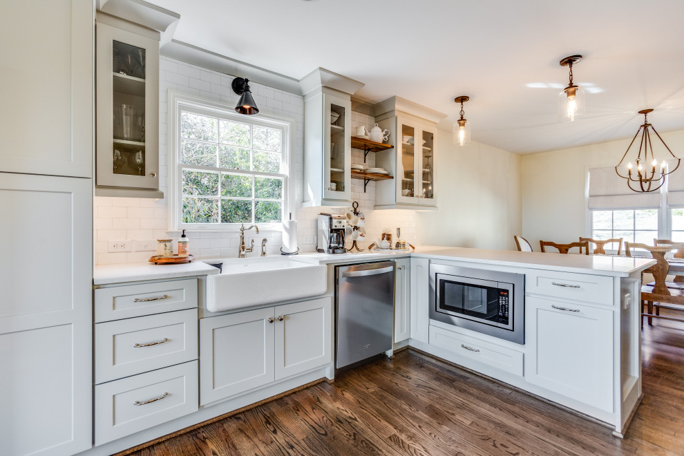 Design ideas for a mid-sized transitional u-shaped eat-in kitchen in Birmingham with a farmhouse sink, shaker cabinets, grey cabinets, quartz benchtops, white splashback, subway tile splashback, stainless steel appliances, medium hardwood floors, a peninsula, brown floor and white benchtop.