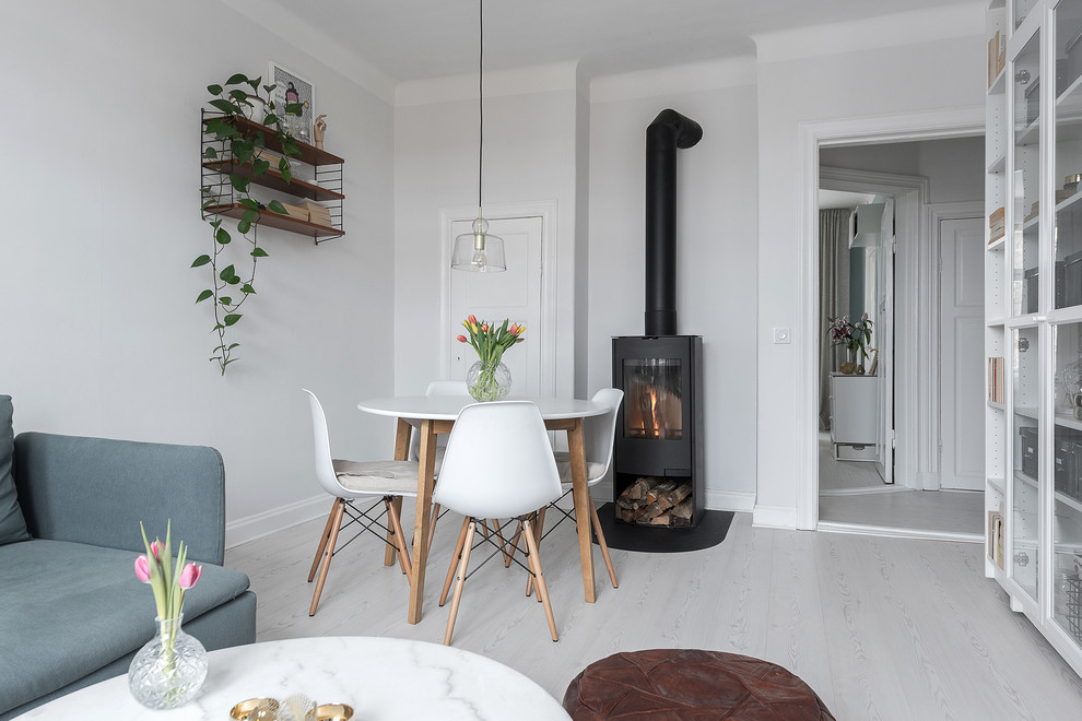 This is an example of a scandinavian dining room in Stockholm with white walls, laminate floors, a wood stove and white floor.