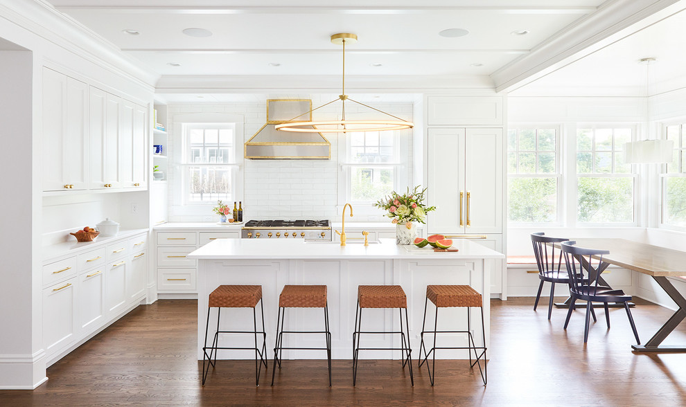 This is an example of a transitional eat-in kitchen in Minneapolis with a farmhouse sink, shaker cabinets, white cabinets, white splashback, subway tile splashback, panelled appliances, medium hardwood floors, with island and brown floor.