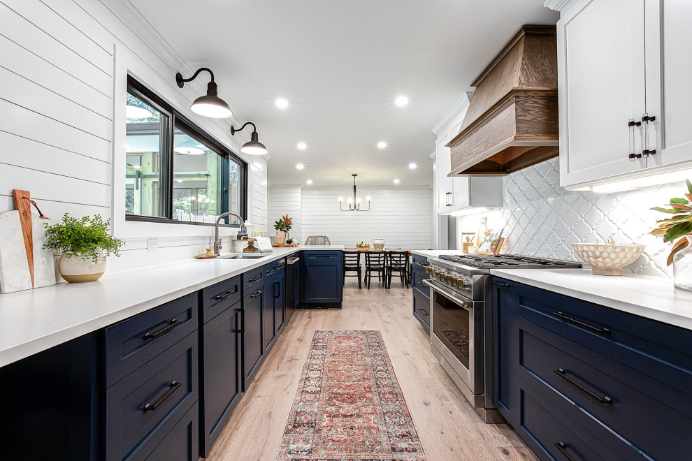 Inredning av ett lantligt mellanstort kök, med en undermonterad diskho, skåp i shakerstil, blå skåp, bänkskiva i kvarts, vitt stänkskydd, stänkskydd i mosaik, rostfria vitvaror och brunt golv