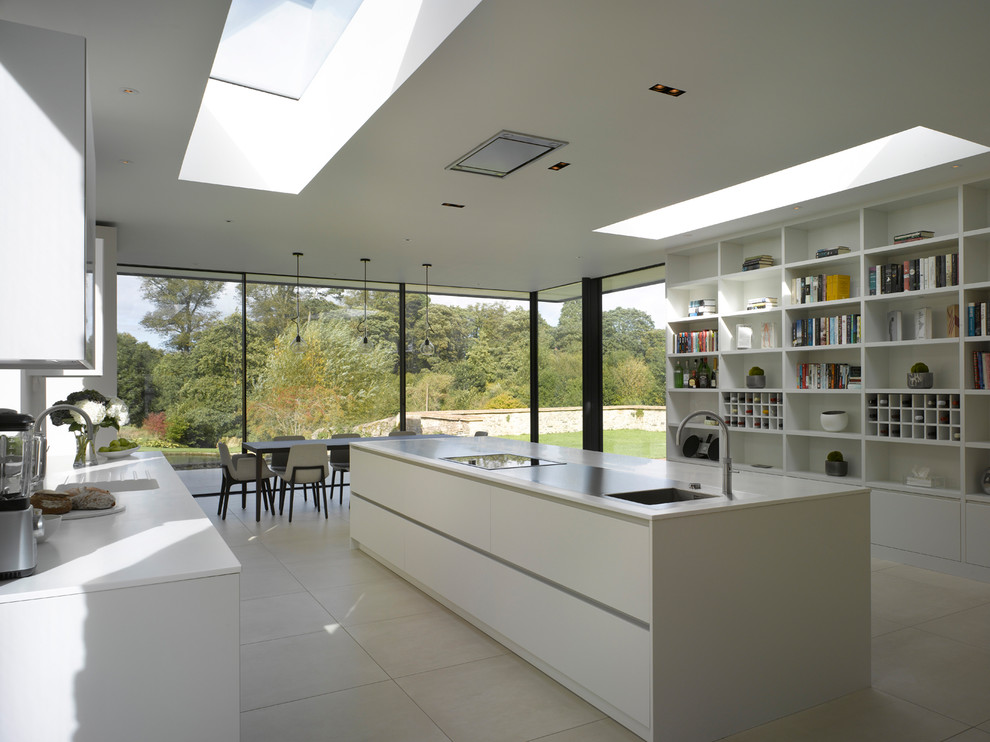 This is an example of an expansive contemporary single-wall open plan kitchen in London with flat-panel cabinets, white cabinets, solid surface benchtops, metallic splashback, mirror splashback, ceramic floors, with island, white floor and white benchtop.