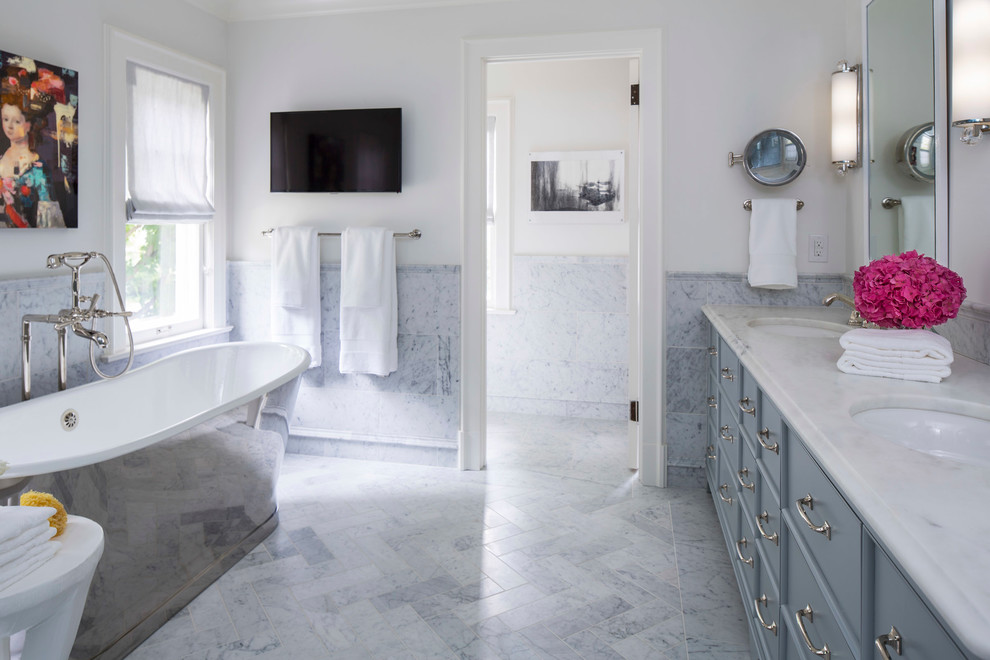 This is an example of a traditional master bathroom in Minneapolis with furniture-like cabinets, blue cabinets, a freestanding tub, multi-coloured tile, marble, white walls, an undermount sink and marble benchtops.