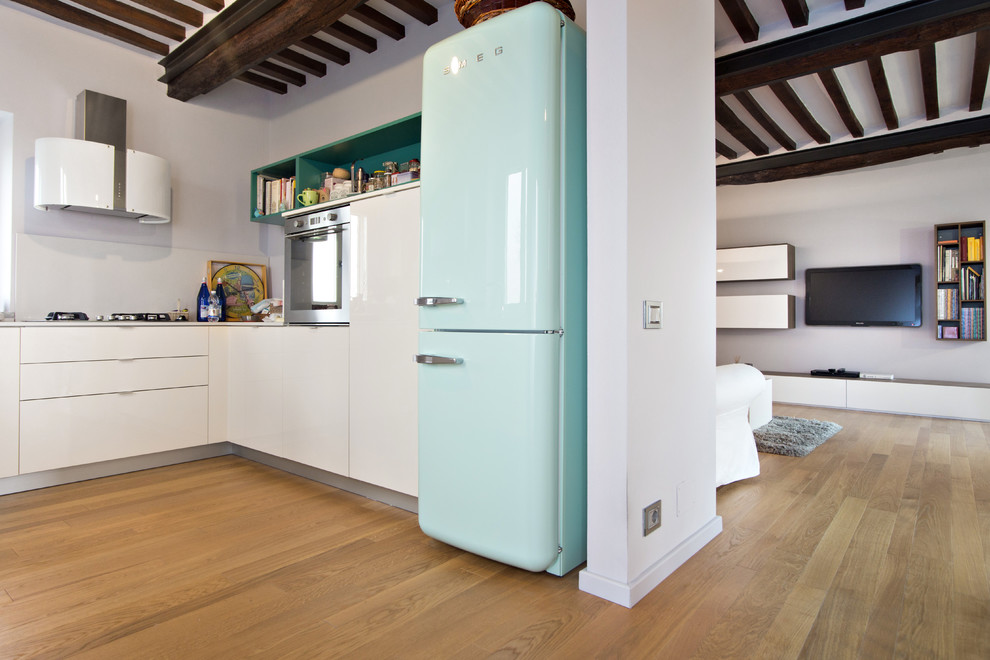 This is an example of a country l-shaped open plan kitchen in Turin with flat-panel cabinets, white cabinets, white splashback, stainless steel appliances and light hardwood floors.