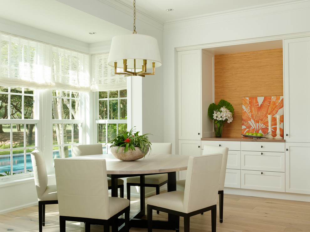 This is an example of a mid-sized tropical dining room in Miami with white walls and light hardwood floors.