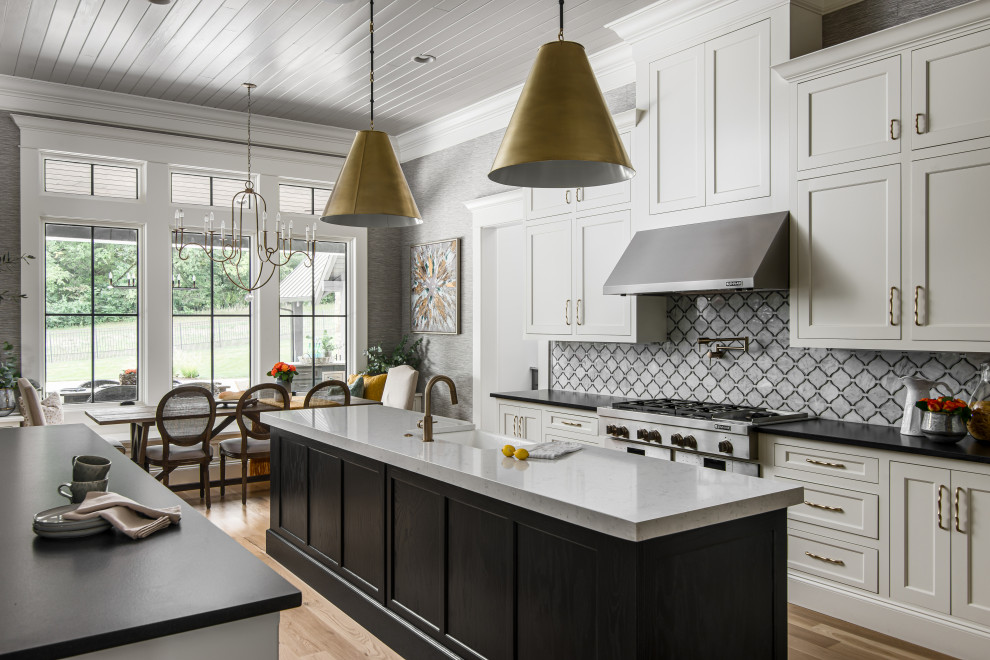 Photo of a large transitional l-shaped open plan kitchen in Nashville with a farmhouse sink, shaker cabinets, white splashback, stainless steel appliances, medium hardwood floors, multiple islands, timber and white cabinets.
