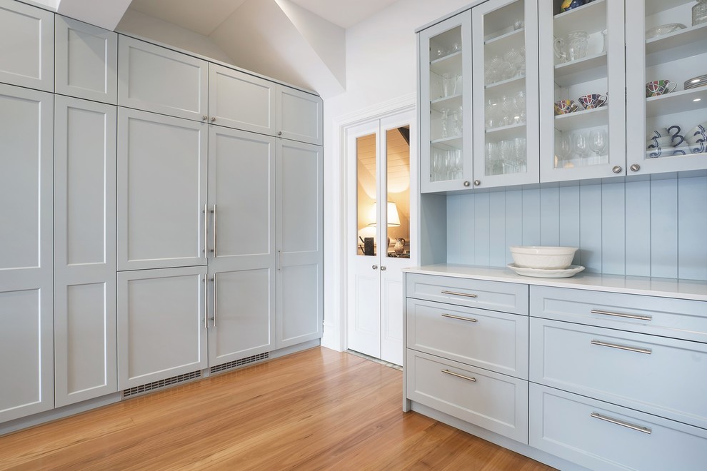 Design ideas for a mid-sized beach style single-wall eat-in kitchen in Sydney with recessed-panel cabinets, grey cabinets, solid surface benchtops, medium hardwood floors, with island, brown floor and white benchtop.
