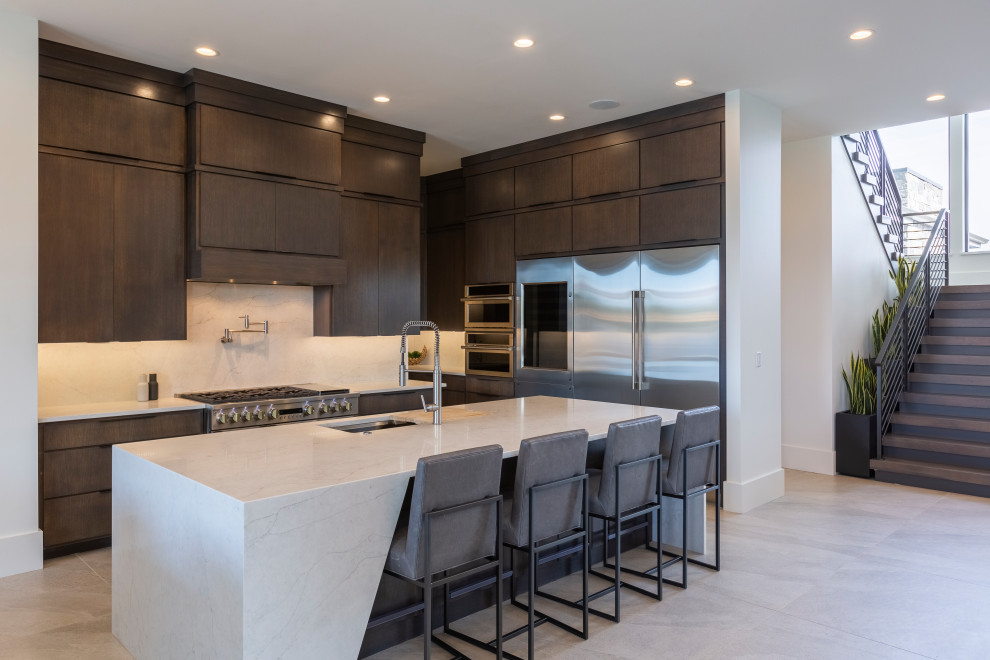 Photo of a contemporary l-shaped kitchen in Omaha with an undermount sink, flat-panel cabinets, dark wood cabinets, white splashback, stone slab splashback, stainless steel appliances, with island, grey floor and white benchtop.