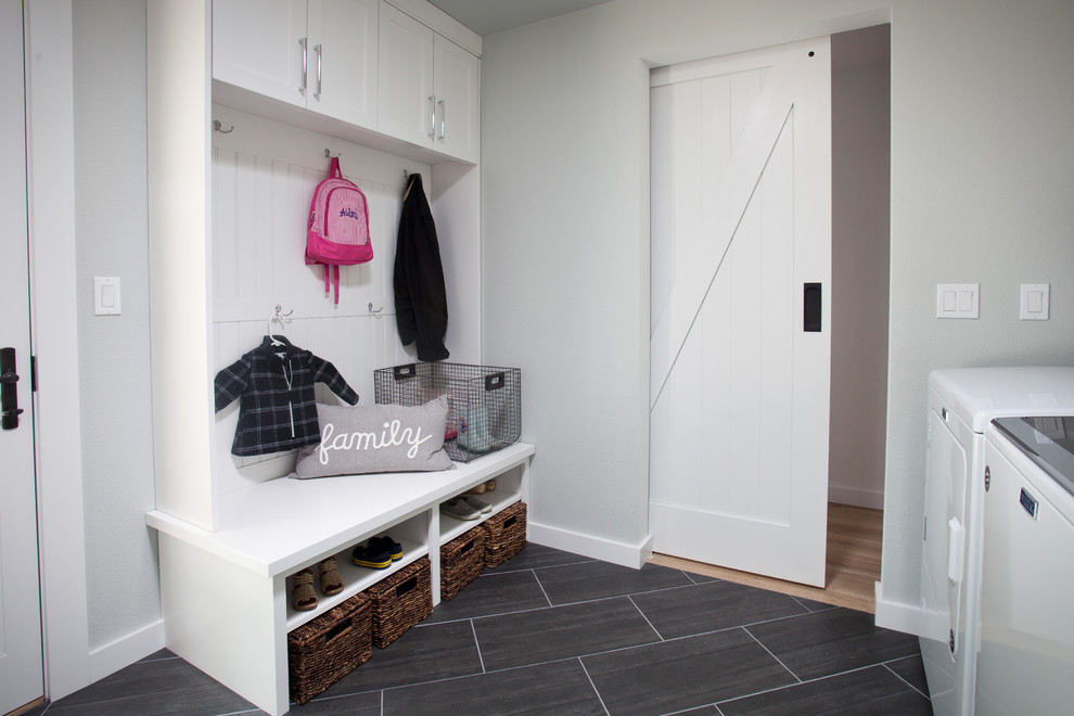 Photo of a mid-sized country utility room in San Francisco with an utility sink, shaker cabinets, white cabinets, white walls, ceramic floors, a side-by-side washer and dryer and black floor.
