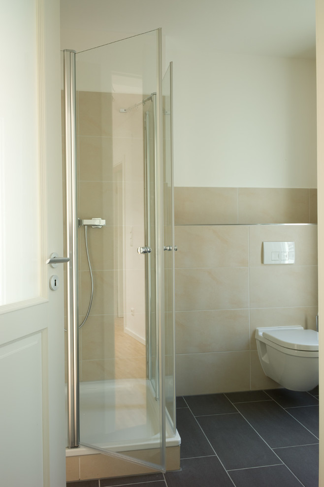 This is an example of a contemporary shower room bathroom in Hamburg with flat-panel cabinets, white cabinets, a corner bath, a corner shower, a wall mounted toilet, beige tiles, stone tiles, white walls and a vessel sink.