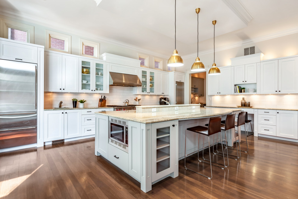 Design ideas for a transitional l-shaped kitchen in Chicago with shaker cabinets, white cabinets, white splashback, stainless steel appliances, medium hardwood floors, with island, brown floor and beige benchtop.
