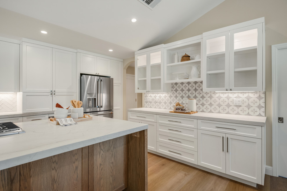 Mid-sized modern u-shaped eat-in kitchen in San Francisco with a farmhouse sink, recessed-panel cabinets, white cabinets, quartzite benchtops, multi-coloured splashback, porcelain splashback, stainless steel appliances, medium hardwood floors, with island, brown floor and white benchtop.