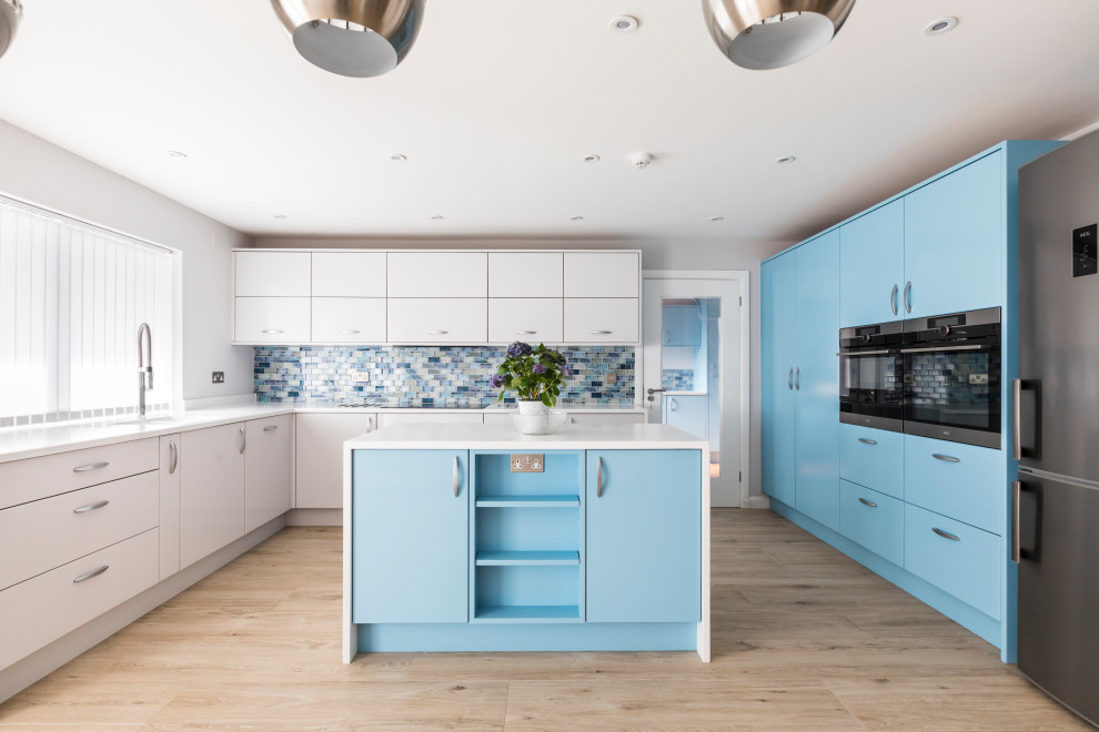 Design ideas for a large contemporary u-shaped kitchen in Dorset with an undermount sink, flat-panel cabinets, blue cabinets, solid surface benchtops, blue splashback, glass tile splashback, porcelain floors, with island, beige floor, white benchtop and stainless steel appliances.