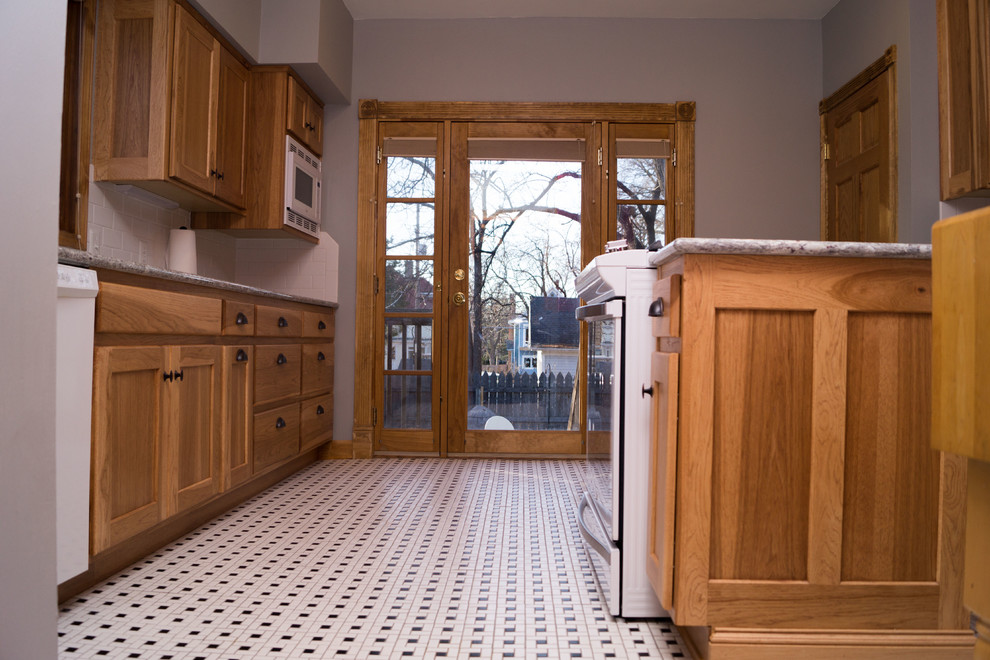 Mid-sized ornate ceramic tile enclosed kitchen photo with an undermount sink, shaker cabinets, light wood cabinets, granite countertops, white backsplash, ceramic backsplash, white appliances and an island