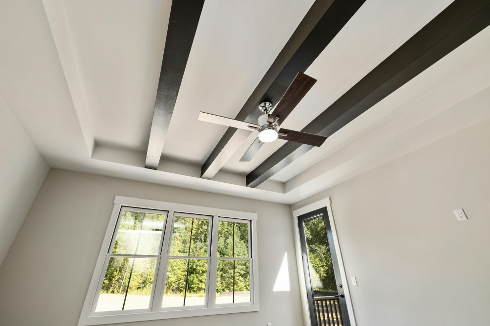 White room in a house with a black ceiling fan and exposed wooden beams