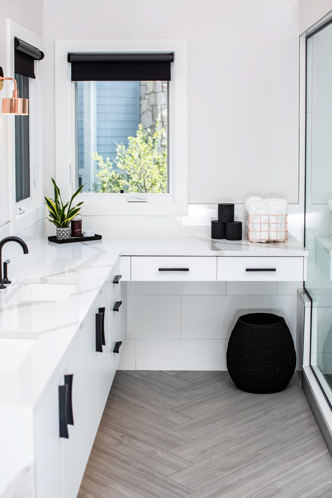 This is an example of an expansive modern master bathroom in Denver with flat-panel cabinets, white cabinets, a freestanding tub, a corner shower, a one-piece toilet, white tile, ceramic tile, white walls, porcelain floors, an undermount sink, engineered quartz benchtops, grey floor, a hinged shower door and white benchtops.