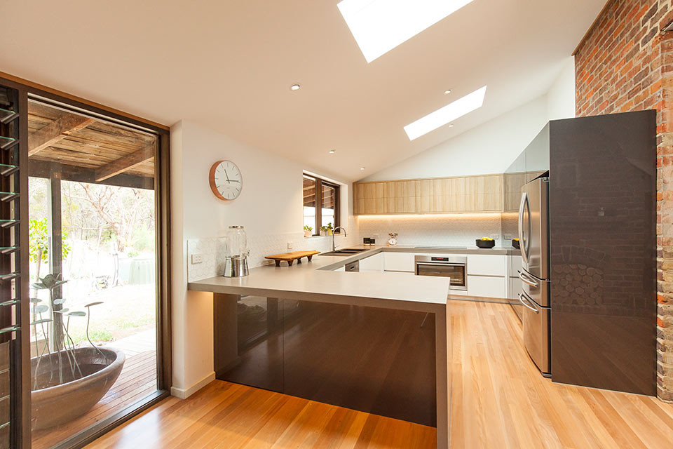 Design ideas for a mid-sized contemporary u-shaped eat-in kitchen in Geelong with a double-bowl sink, flat-panel cabinets, white cabinets, quartz benchtops, white splashback, ceramic splashback, stainless steel appliances, light hardwood floors and no island.